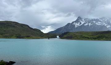 Turquoise lake surrounded by hills with snowy mountains in the distance.