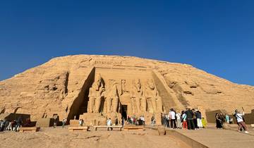 Abu Simbel monumental statues and visitors under clear blue sky.