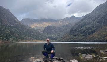 Person posing in front of a lake surrounded by mountains.