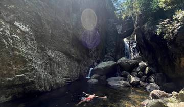 Person swimming in a water pool within rock formations.