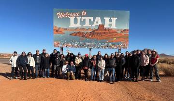 Large group posing in front of the Utah welcome sign.