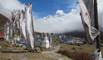 Prayer flags and a mountain village overlooking a snow-capped peak.