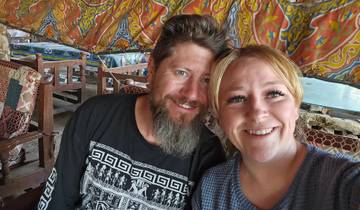 Two people smiling inside a colorful, patterned tent.
