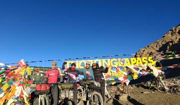 Cyclists posing at the summit of a mountain pass with flags and sign.