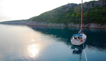 Sailboat anchored in a calm bay at sunset, with a rocky shoreline and tranquil water.
