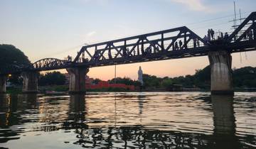 Bridge over a river with a large statue in the background during sunset.
