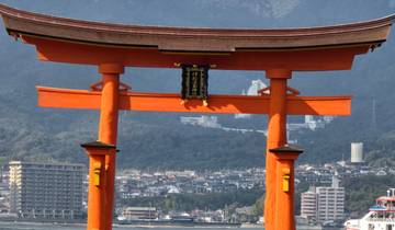 Iconic red torii gate in front of a cityscape and mountains.