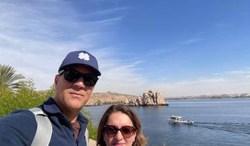 Couple posing by a river with a boat and rocky landscape.