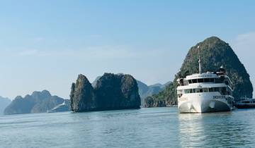 A large ship cruising near limestone formations in a bay.