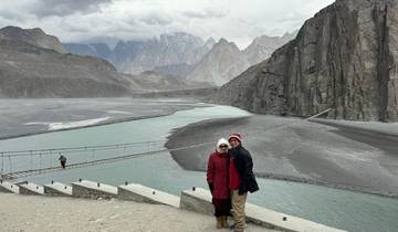 Couple posing in front of a scenic mountain river with a suspension bridge.