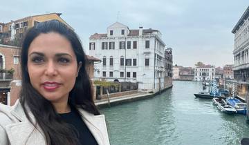 Person posing next to a canal with buildings in the background.