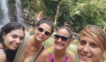 Group of women smiling at a waterfall with other people around.