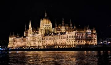Night view of a brightly lit historic building with a reflection on water.