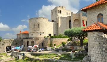 Large stone castle with tourists walking nearby.