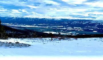 Vast snowy landscape with distant mountain ranges under a dramatic sky.