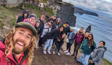 A group photo with smiling people and the Cliffs of Moher in the background.
