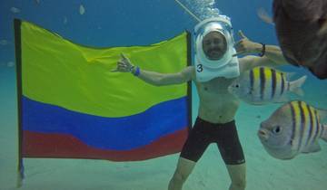 Person underwater with a helmet, a Colombian flag, and fish swimming around.