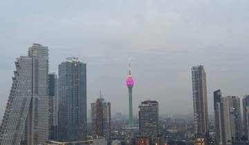 Skyline of a city with a prominent lit-up tower at dusk.