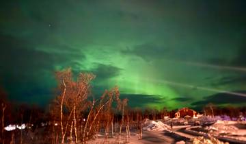 Aurora borealis over snowy landscape with a house visible.