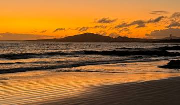 Beautiful sunset over a beach with a lighthouse and ocean waves.