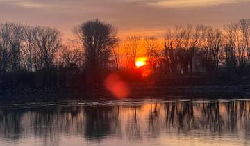 Sunset over a river with silhouetted trees.