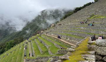 Terraced ruins with people walking on the pathway, surrounded by mist.