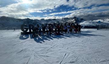 People standing near a sign on a snowy mountain with dramatic scenery.