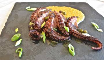 Close-up of a gourmet octopus dish with garnish on a slate platter.