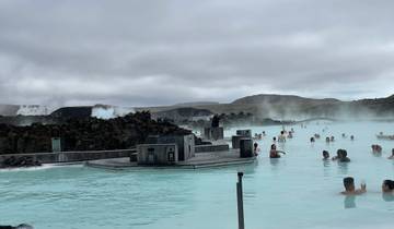 People relaxing in a geothermal spa with mountainous background.