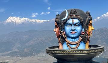 Three-faced Shiva statue with mountains in the background.