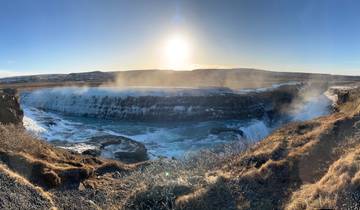 A panoramic view of a waterfall with sunlight and mist.