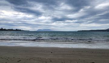 Cloudy sky above a calm sea viewed from a sandy beach.