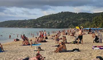 Crowded beach with people sunbathing and swimming.
