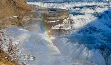 Waterfall with snow and a rainbow in the mist.