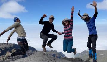 Group of people jumping on a mountain with clouds below.