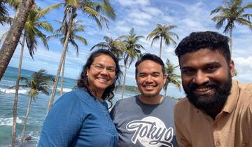Three people smiling in front of tropical palm trees with ocean view.