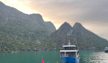 Boat on calm water with jagged cliffs and lush greenery in the background.