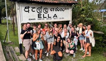 A group of tourists posing in front of a sign for Ella.