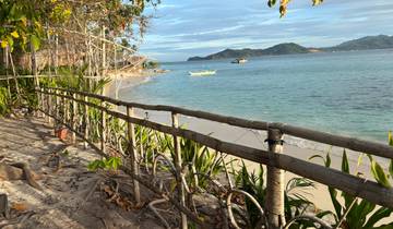 Scenic beach with a wooden fence and distant boats.