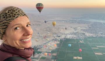 A person in a hot air balloon over a landscape with other balloons.