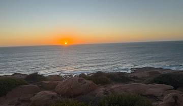 Sunset over the ocean with a rocky coastline.