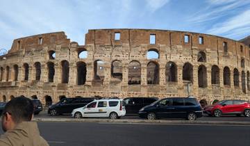 Large ancient amphitheater with vehicles parked outside.