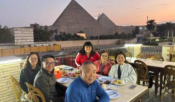 Group of people dining outdoors with the pyramids in the background during sunset.
