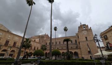 Historic building with clock tower and palm trees under a cloudy sky.