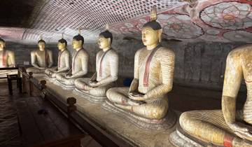 Row of ancient, seated Buddha statues inside a cave with painted ceilings.