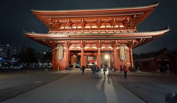 Visitors at a brightly lit temple gate at night.