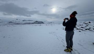 A person photographing a snow-covered landscape with distant mountains.