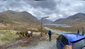 People enjoying a scenic view of a valley with a blue car nearby.