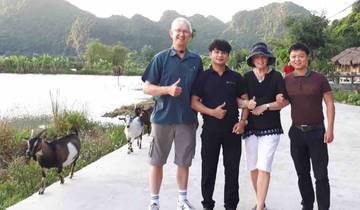 Four people posing with thumbs up in a rural landscape with goats.