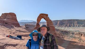 Two people posing in front of Delicate Arch in a desert landscape.